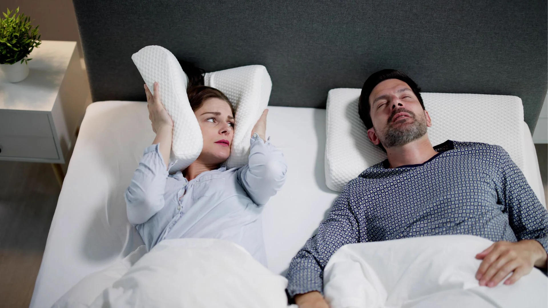 a wife covering her ears as her husband snores