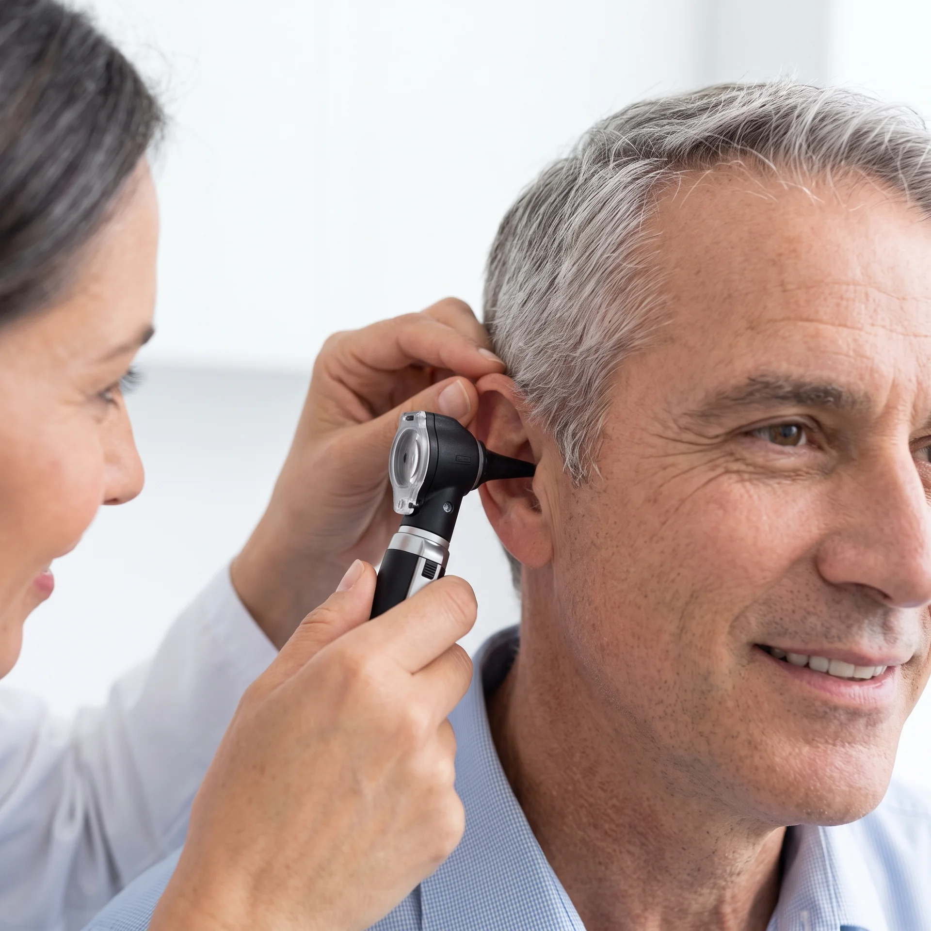 A caring specialist examines a 50+ year old patient's ear with an otoscope in a clean medical office.
