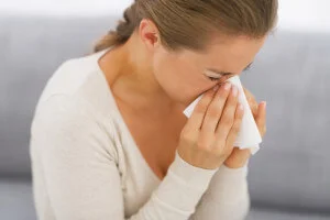 Young woman sitting on couch and blowing nose