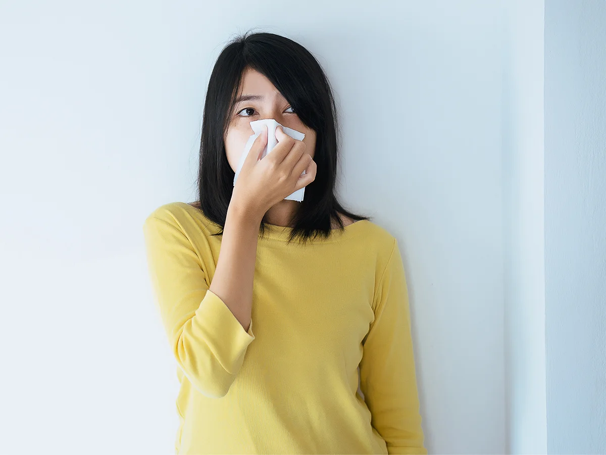 Woman in yellow sweater holding tissue to her nose